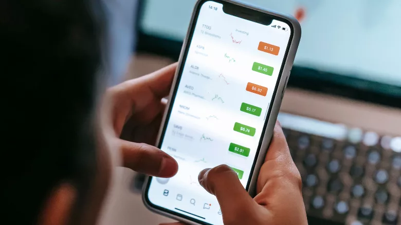 A person using their phone in front of a computer screen.