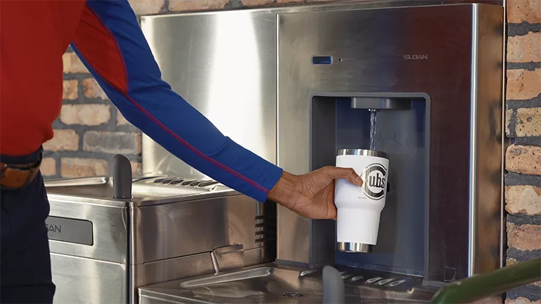 A person wearing a Cubs shirt refilling a "Cubs" cup at a Sloan bottle filler.