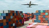 A plane flying over several colorful shipping containers. 