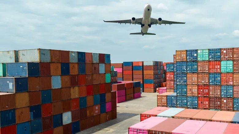 A plane flying over several colorful shipping containers. 