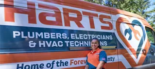 A woman standing in front of a Harts Plumbing, Electricians & HVAC Technicians truck.