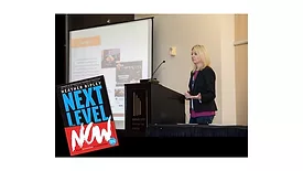 Heather Ripley addressing a crowd, with her book "Next Level Now."