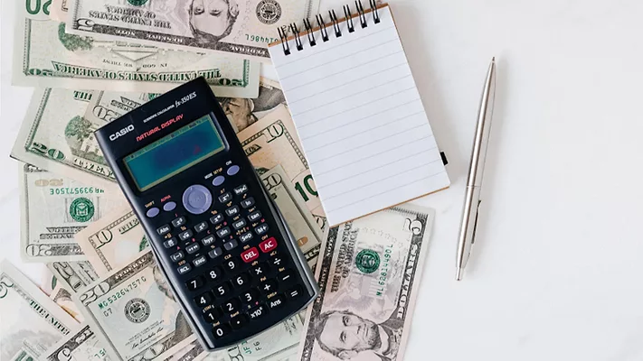 A calculator, notepad and pencil over money. 