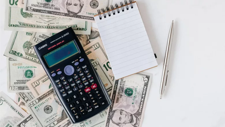 A calculator, notepad and pencil over money. 