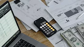A desk with a computer, phone, money and documents. 