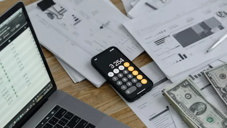 A desk with a computer, phone, money and documents. 