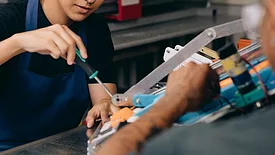 A young technician's hands working on a project while an older technician helps. 