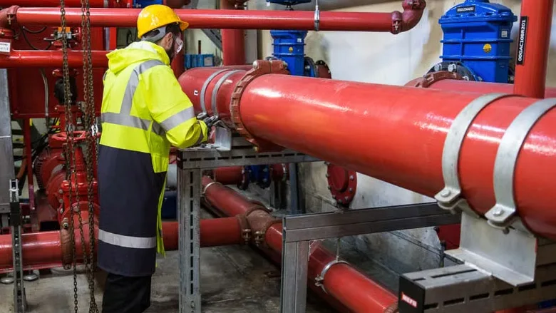 An Open & Shut Case (Part 2) Engineer with safety gear inspecting red industrial piping system indoors.