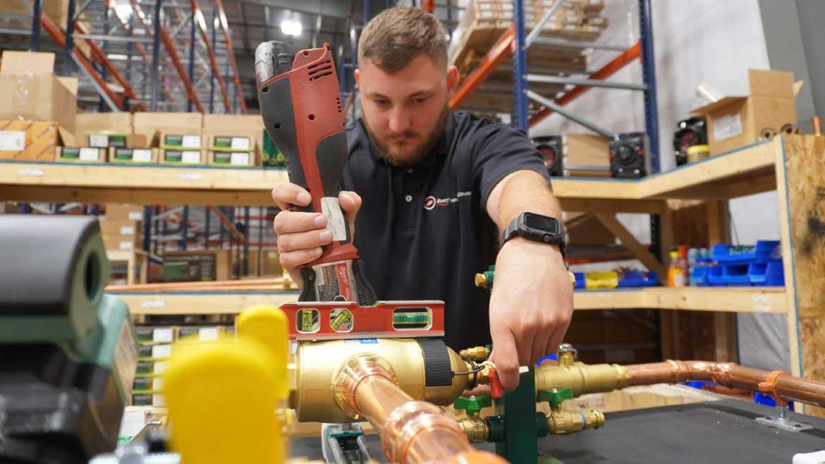 04 PM 1223 FW Webb feature. Jared Dodge, F. W. Webb Lead Boiler Board Technician uses a level to install near-boiler piping components on a boiler board.