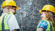 PM March 2024 Kenny Chapman column feature image of mature male and young female building workers smile together