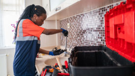 Black female Plumber fixing a leak in the kitchen sink of a house