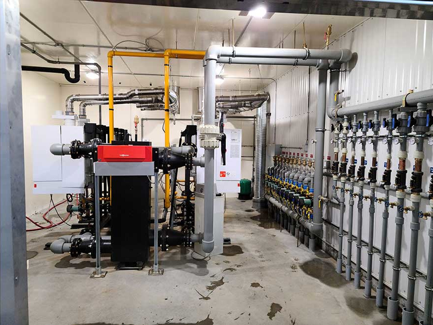Multi-boiler cascade system mounted to the floor in the center of the room, with a collection of Taco zone pumps on the wall.