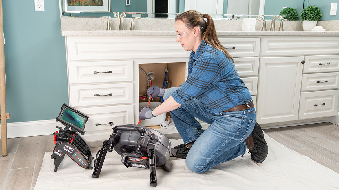 RIDGID SeeSnake microReel APX with TruSense being used in a kitchen under the sink by a female plumber.