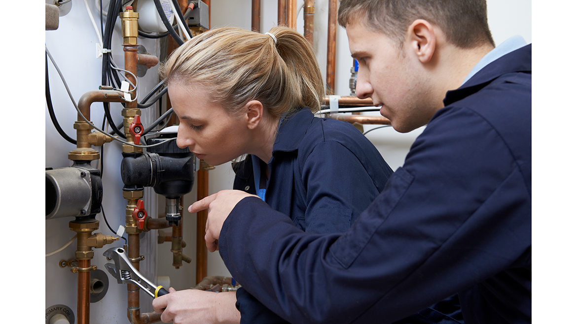Female Trainee Plumber Working On Central Heating Boiler