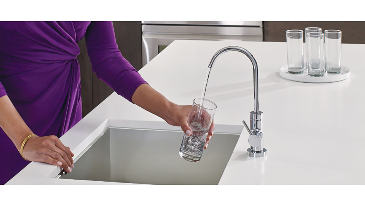 Woman in purple dress filling a glass with filtered water from a faucet.