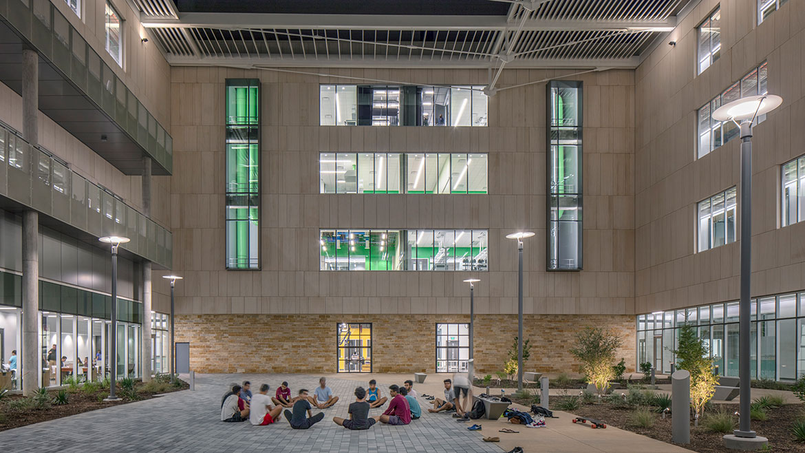 Interior courtyard with glass wall panels with students sitting in a circle.