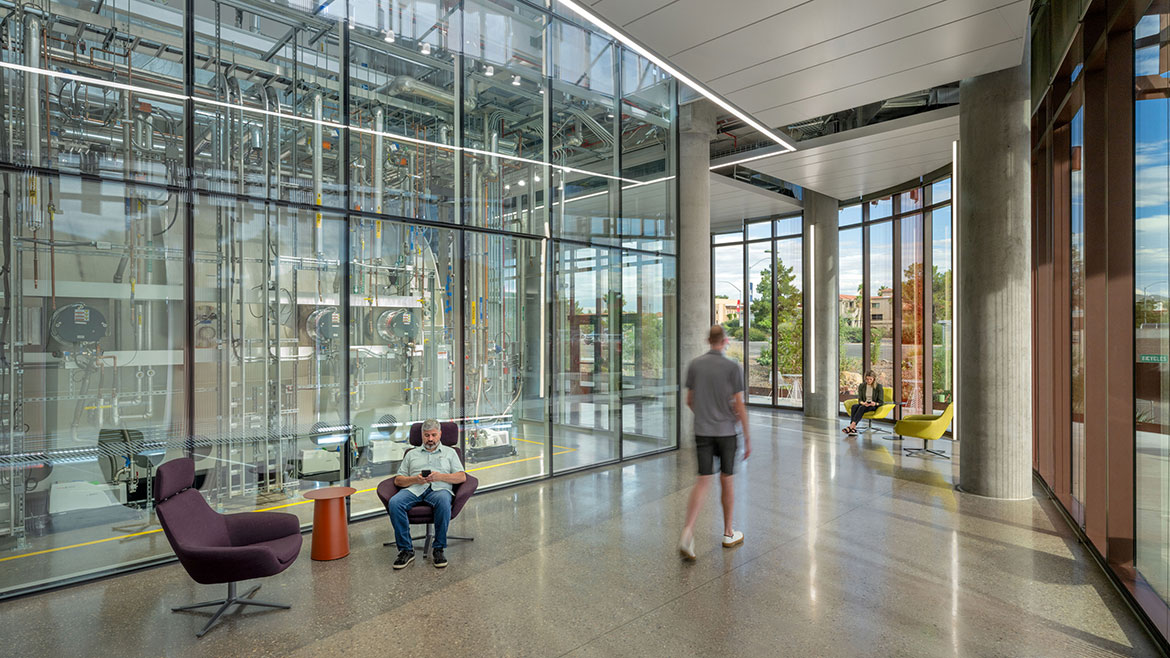 University of Arizona’s Applied Research Building Thermal Vacuum Chamber. Two people are sitting on chairs and a man (blurry) is walking past them.