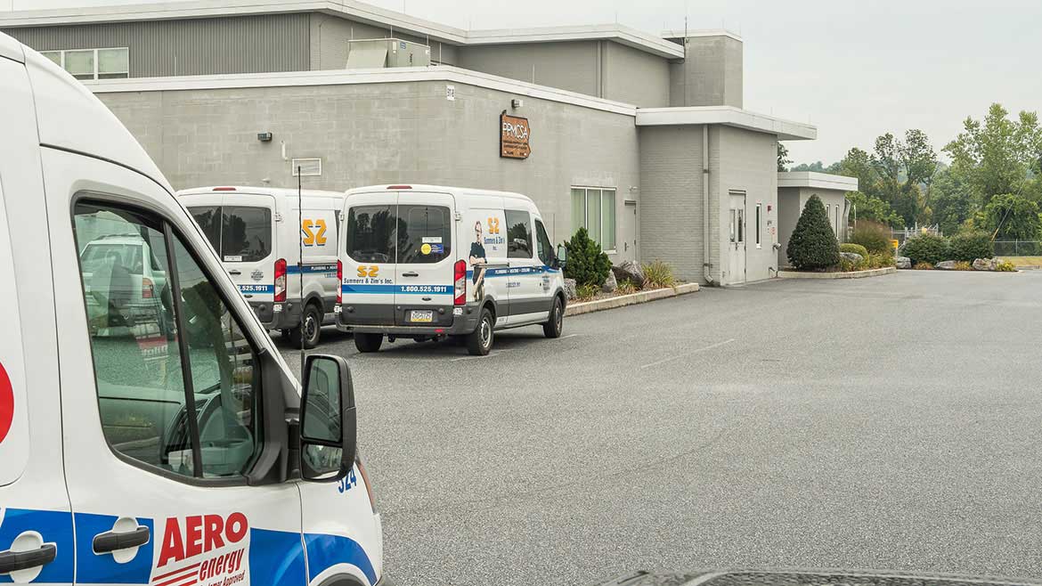 Exteror of PPATEC building with several work vans parked outside.