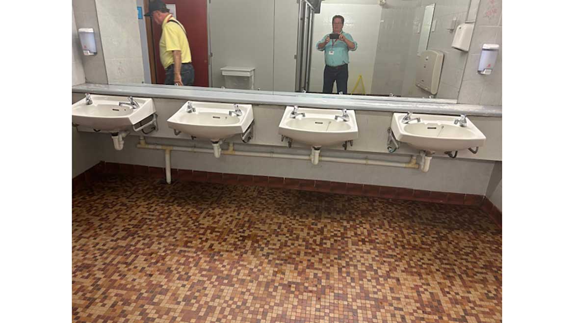 Bank of lavatories, two men in the mirror's reflection, one leaving and another taking the photo.