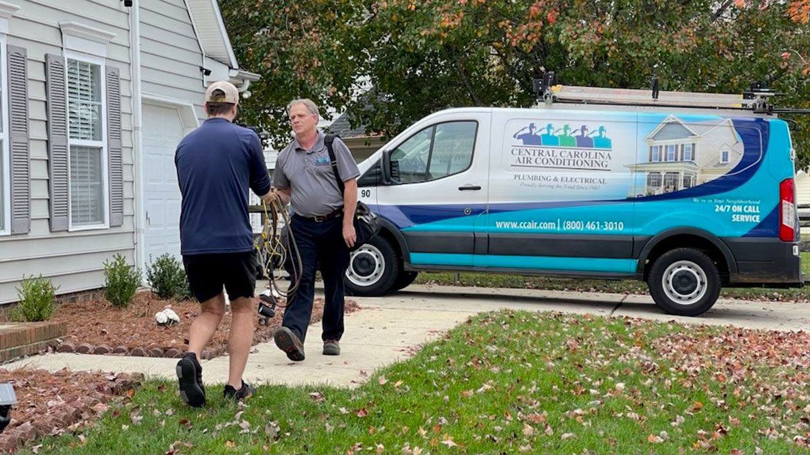 Central Carolina Air Conditioning van in the background while a contractor is being videotaped walking towards the front door of a house.