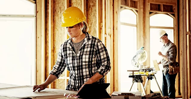 Woman architect looking over blueprints at home construction site.