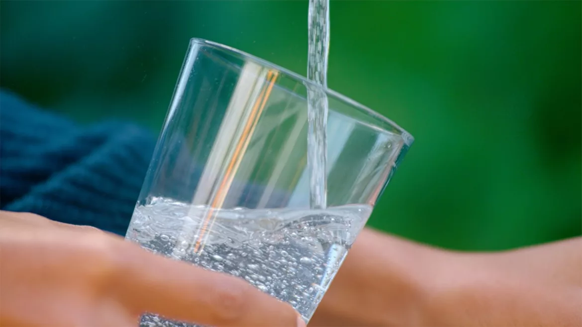 Water being poured into a glass. Close up of person holding the glass and a blurred background.