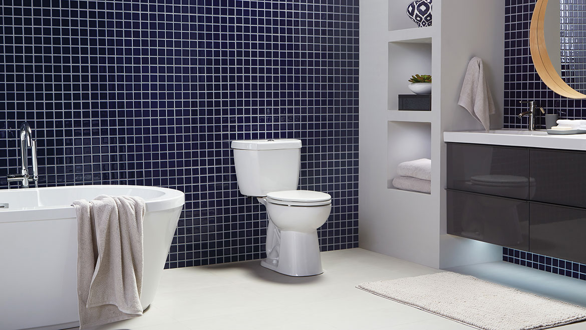 A large bathroom with small dark tiles on the wall, a freestanding bathrub on the left and a Niagara 0.8 GPF toilet with patented Stealth Technology® in the center.