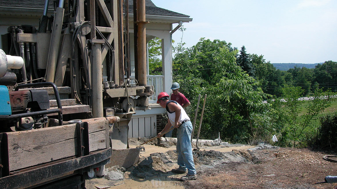 Two men wearing hard hats working with a GSHP installation driller.