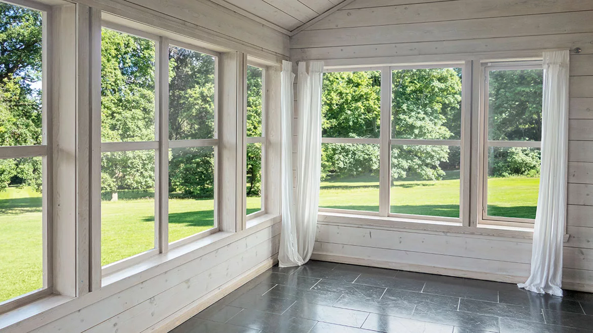 Empty modern room with large windows looking out onto a green lawn and trees.