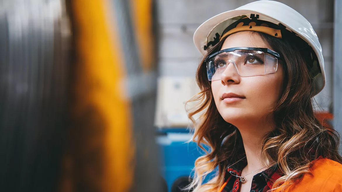 She's wearing a white safety helmet and safety glasses.