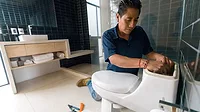 Latin American plumber fixing a toilet in the bathroom.
