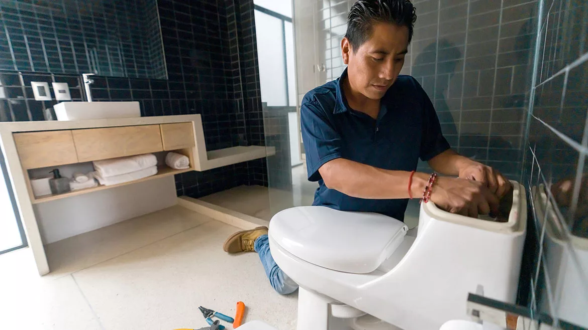 Latin American plumber fixing a toilet in the bathroom.