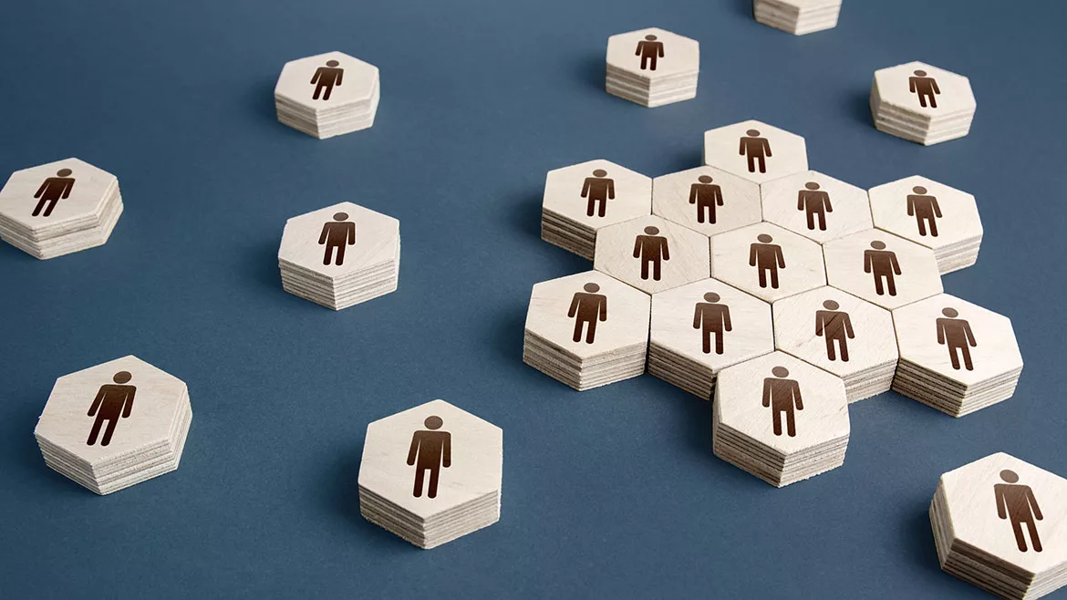 Hexagon-shaped wooden pieces with a human figure in black in the center. Some pieces are placed together with single pieces around it on a blue table.