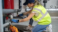 Female technician repairing heating system pipes in the boiler room.