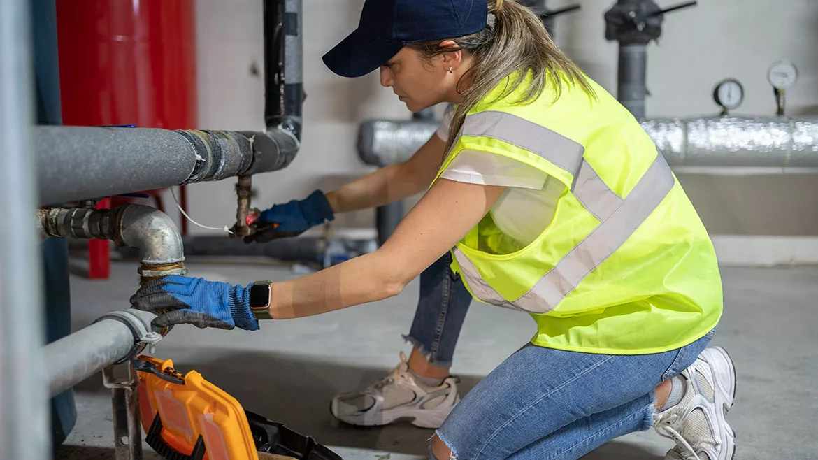 Female technician repairing heating system pipes in the boiler room.