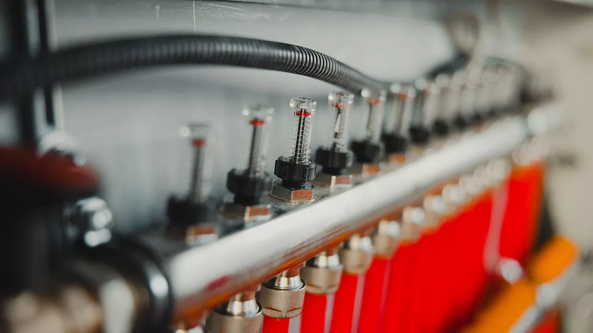 Close-up of a manifold with flow meters regulating water pressure in an underfloor heating system, ensuring efficient temperature control.