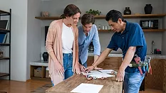 Plumber fixing a pipe and talking to his clients in the kitchen.