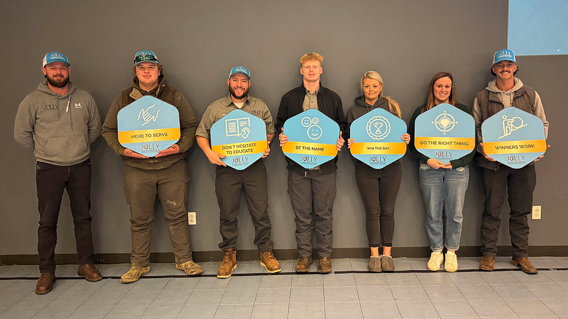 Team member winners of Jolly's Town Hall awards posing against a wall with signs.