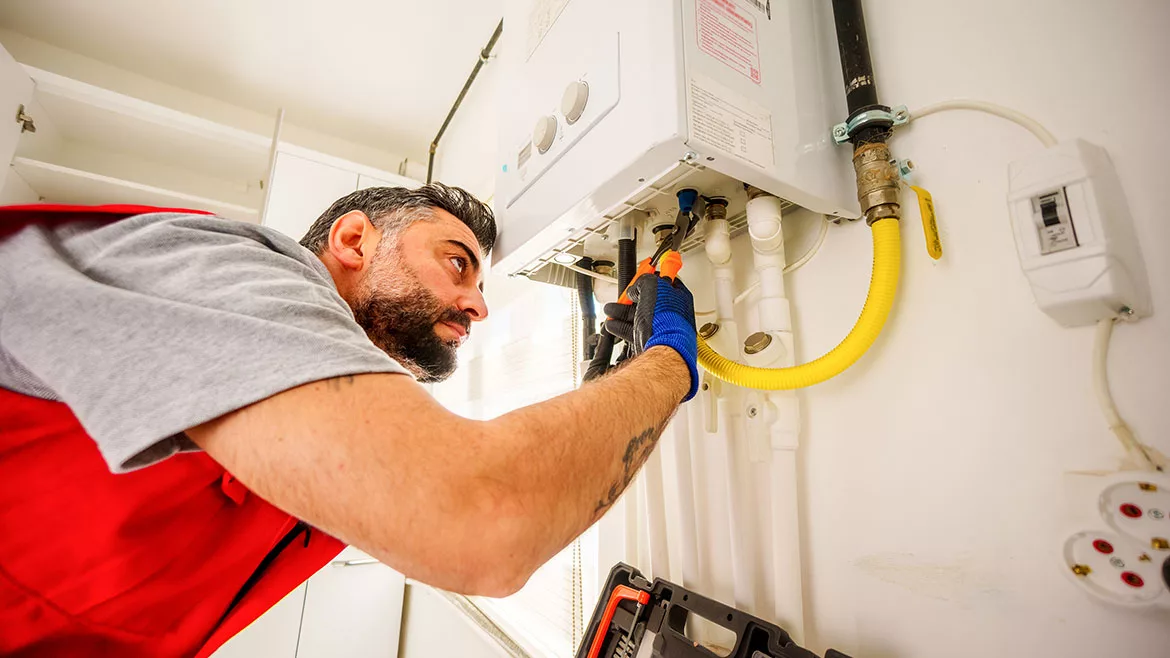 Bearded plumber uses a wrench to repair a gas boiler.