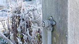 Close up of outdoor water tap covered in frost, attached to a wooden post on an allotment garden in winter.