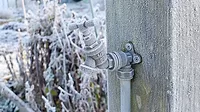 Close up of outdoor water tap covered in frost, attached to a wooden post on an allotment garden in winter.