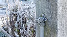 Close up of outdoor water tap covered in frost, attached to a wooden post on an allotment garden in winter.