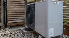 Side view of the air source heat pump outside in the garden, near wooden fence on a sunny day.