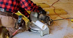 A plumber cutting PVC pipe with a band saw at a construction site.