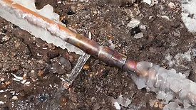 Frozen Cracked Copper Water Main Pipe Leaking A 3/4" copper water main has frozen and cracked below ground outside a house. The background is excavated dirt.
