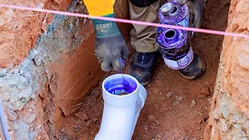 Cropped image of a plumber putting glue on the inside of a PVC pipe in a trench.