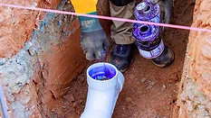 Cropped image of a plumber putting glue on the inside of a PVC pipe in a trench.
