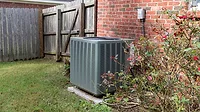 Air Conditioner system next to a home Air conditioner condenser unit sitting next to brick home with fence.