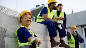 Team of construction workers in bright safety vests and helmets taking a break together outdoors.