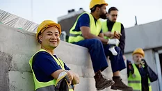 Team of construction workers in bright safety vests and helmets taking a break together outdoors.